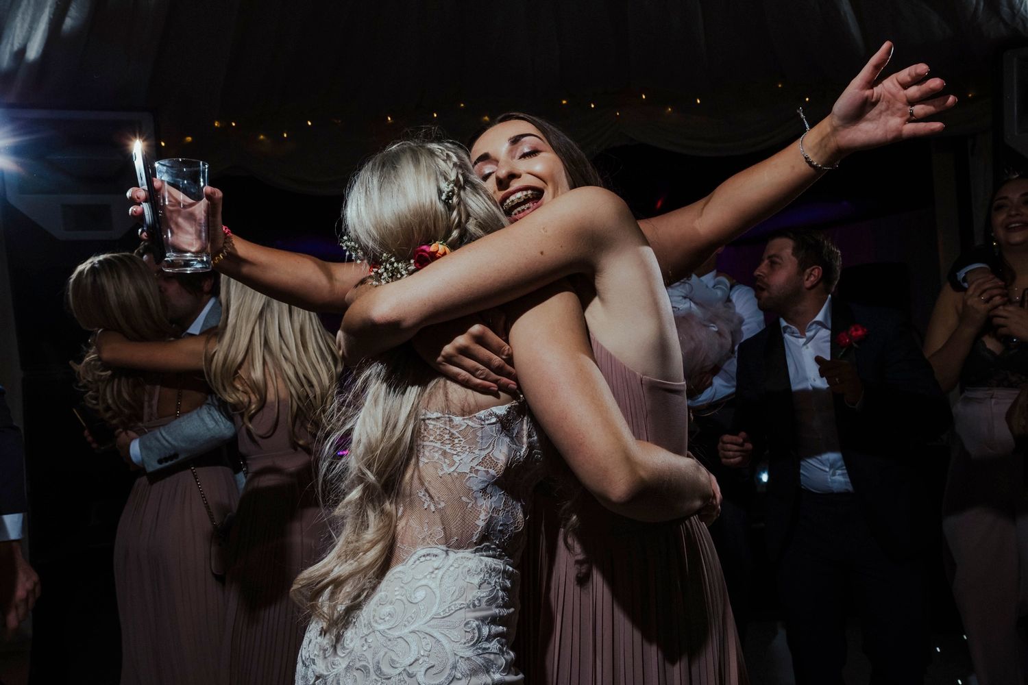 Two wedding guests sharing an enthusiastic embrace on the dance floor at night.