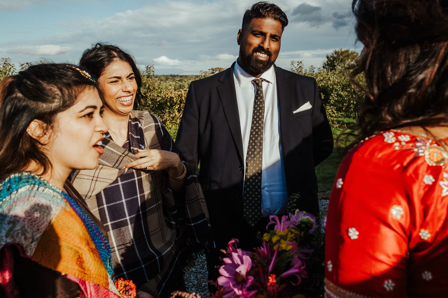 Guests mingling at an outdoor fusion wedding celebration against a natural landscape.