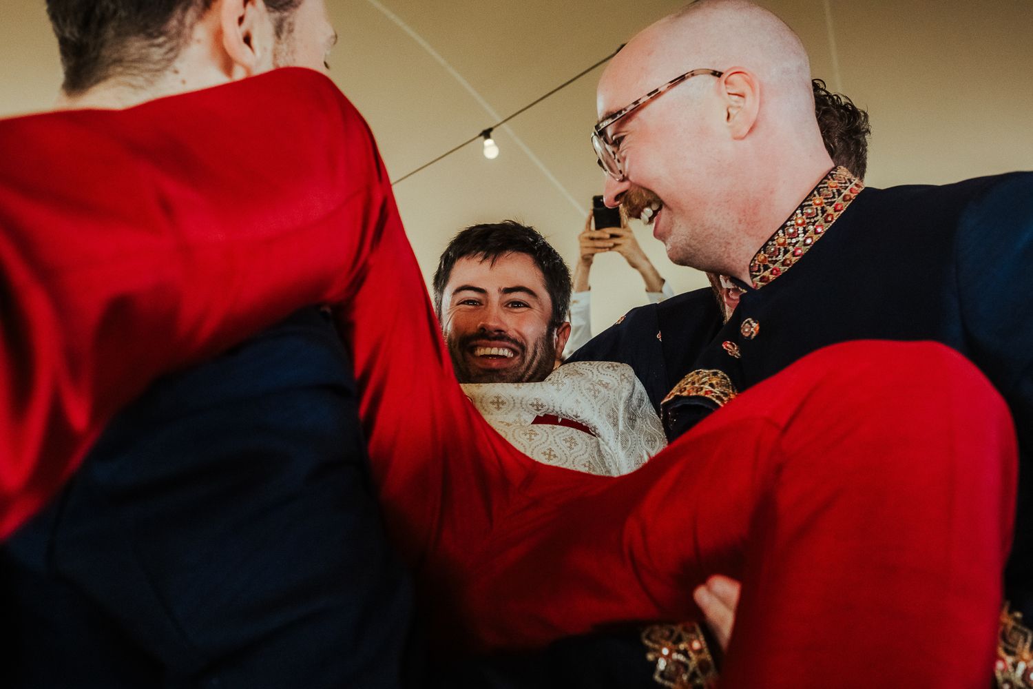 Wedding guests in traditional Scottish attire laugh and embrace during celebrations.