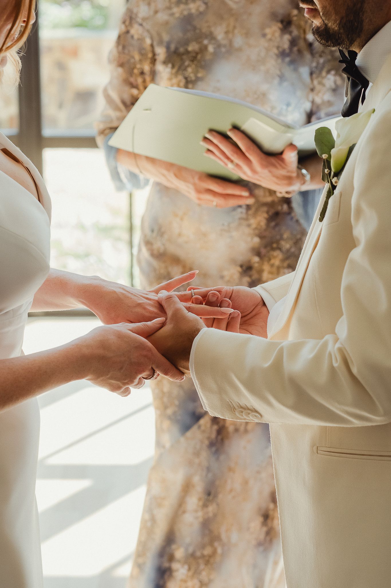 Close-up view of hands exchanging wedding rings during an intimate ceremony in natural lighting.