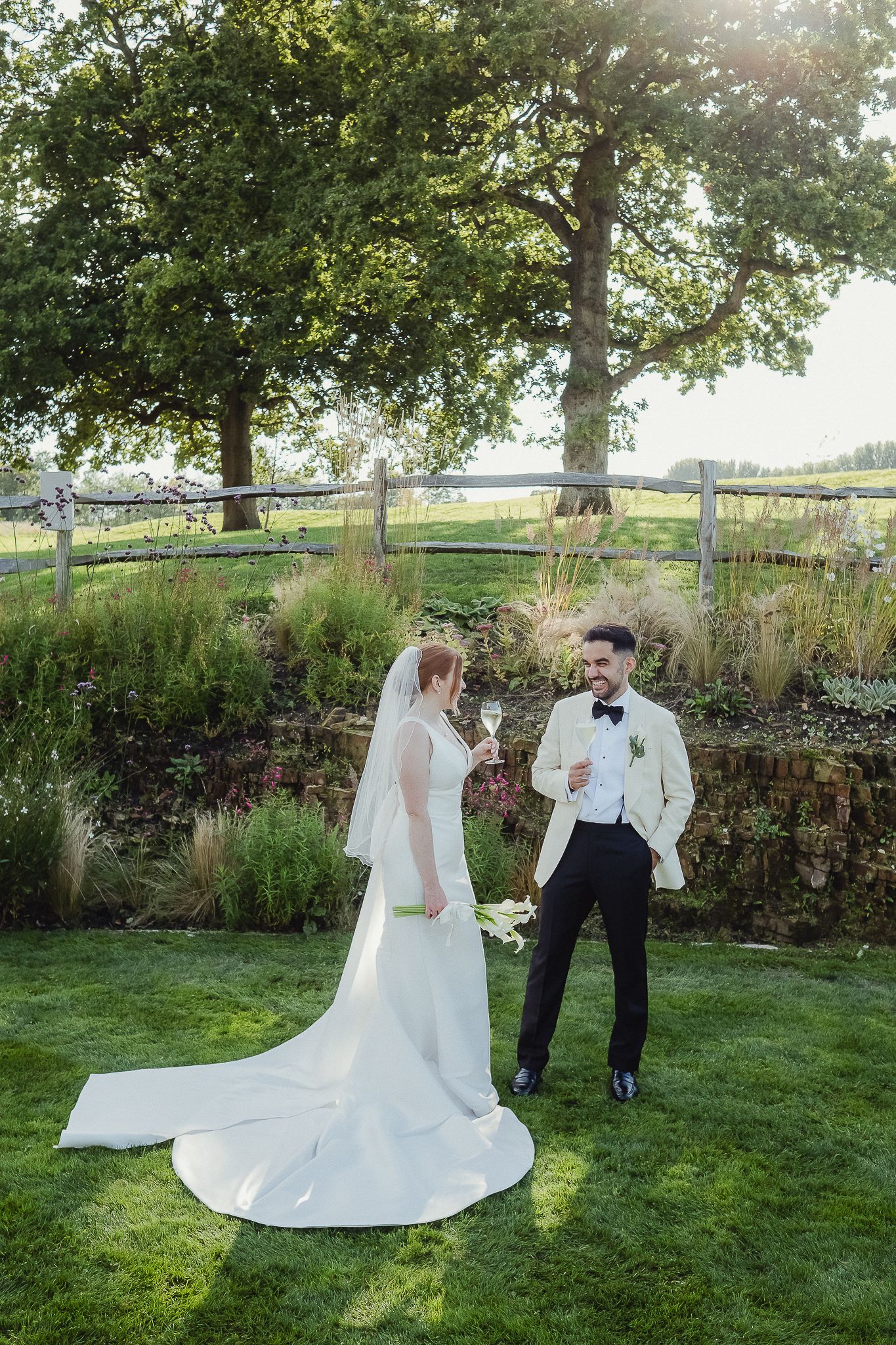 A couple shares a romantic moment in an outdoor garden setting with lush trees and greenery on a sunny afternoon.