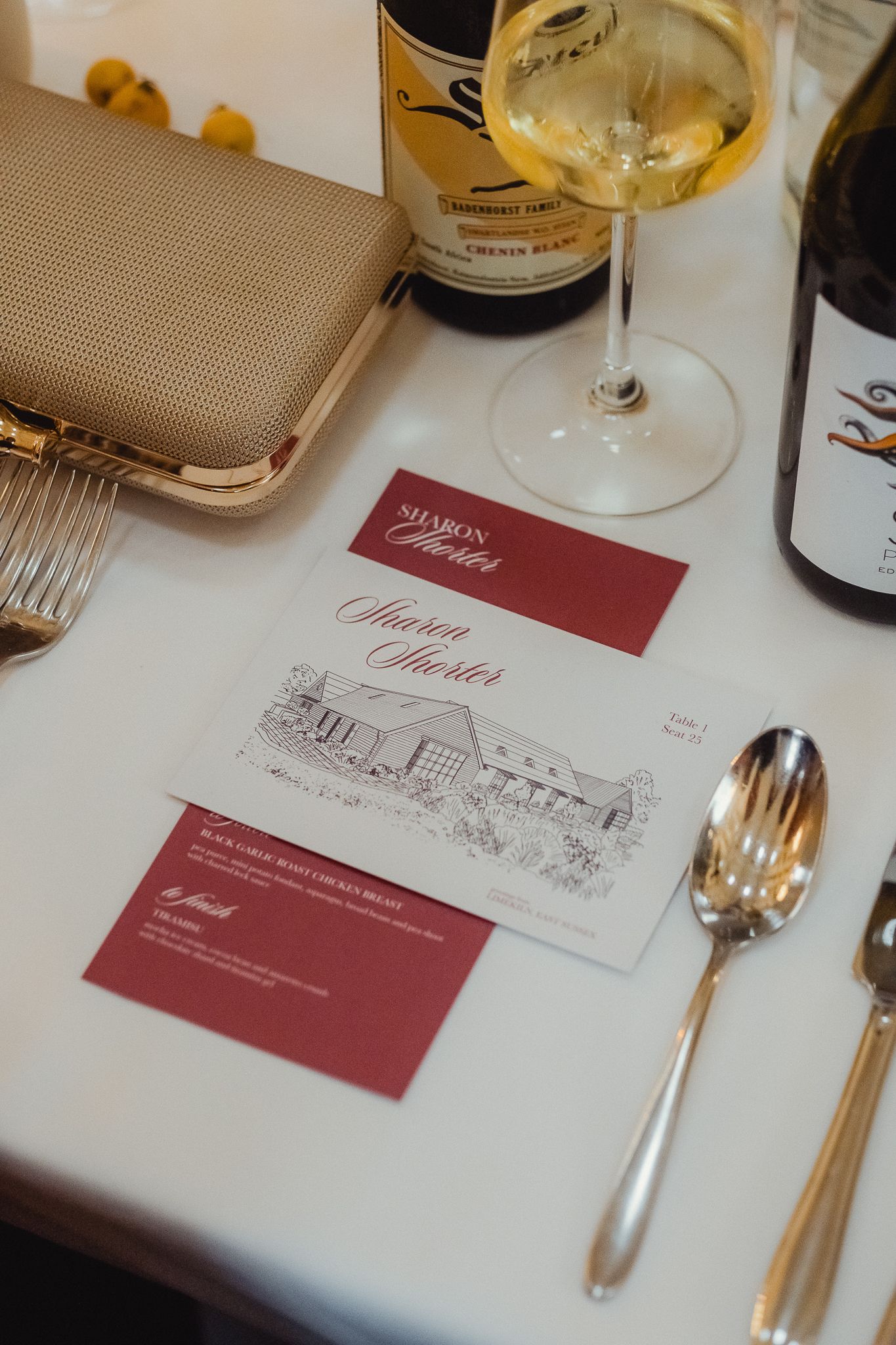 Wedding reception place settings with burgundy menus and wine glasses on a white tablecloth.