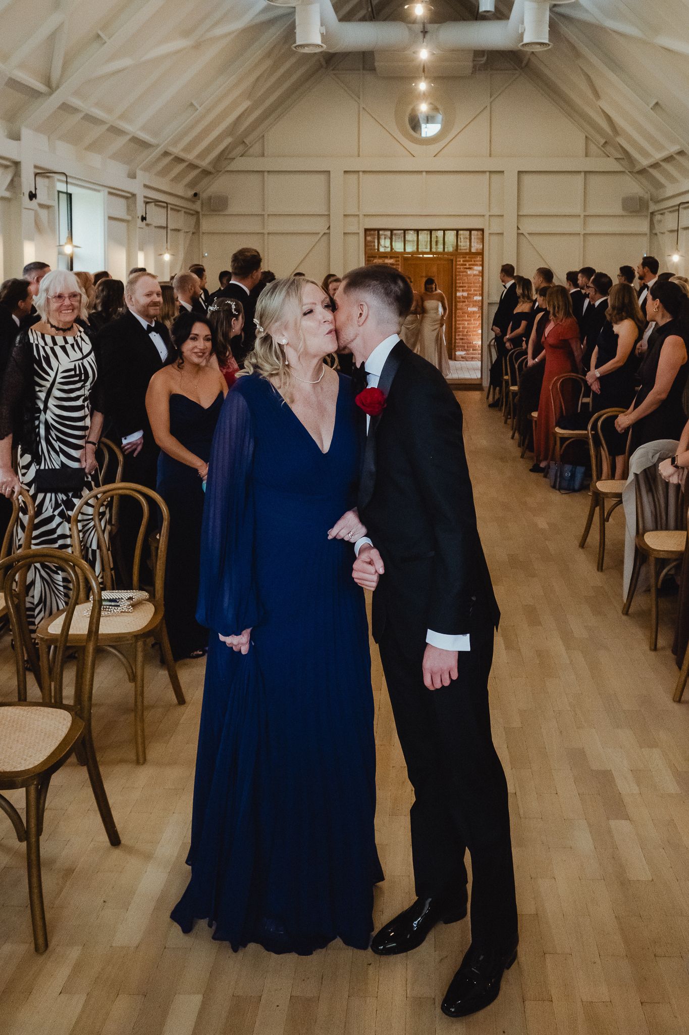Couples dancing and socializing at an elegant indoor reception with hardwood floors and warm lighting.