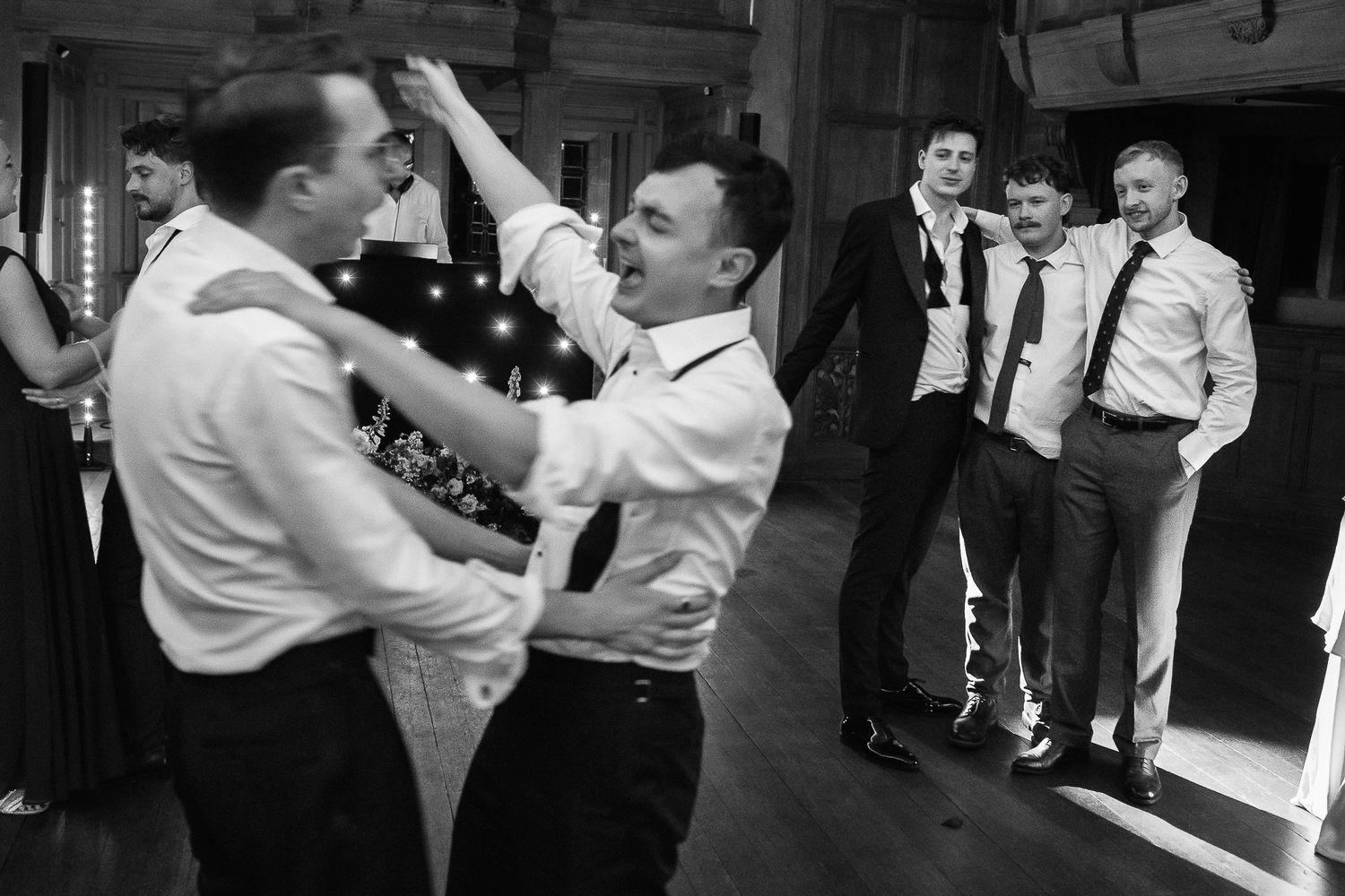 Black and white photo of men dancing and laughing at a wedding reception party celebration.