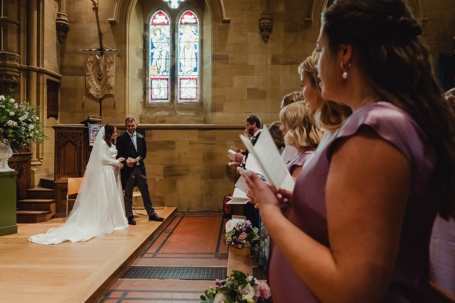 Wedding ceremony taking place in a grand stone church with stained glass windows and traditional architecture.