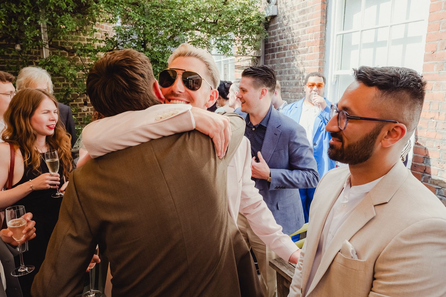 A group of people mingling and socializing at an indoor event with brick walls and natural lighting.