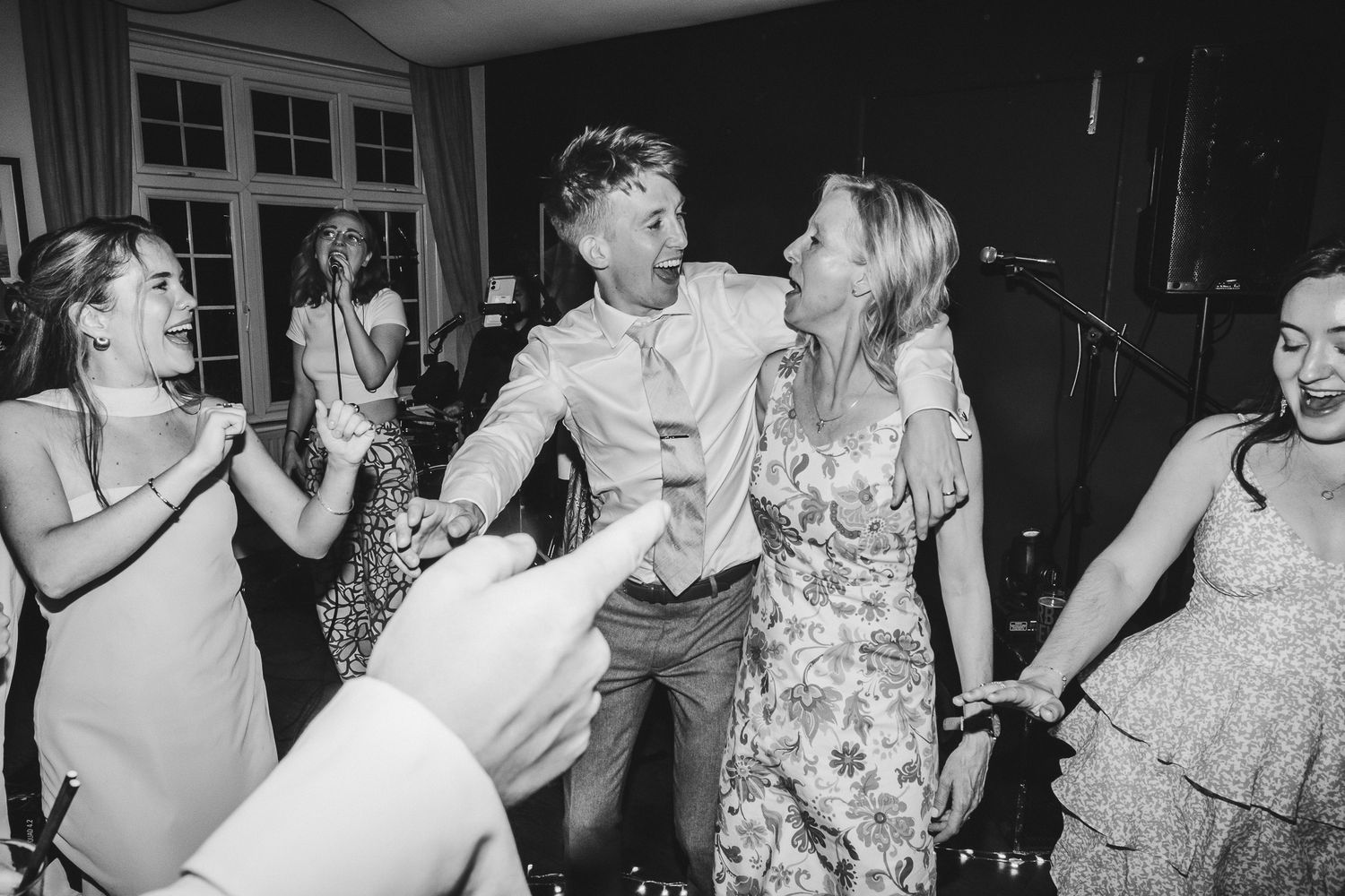 Black and white photo of people dancing and celebrating at what appears to be a wedding reception or party.