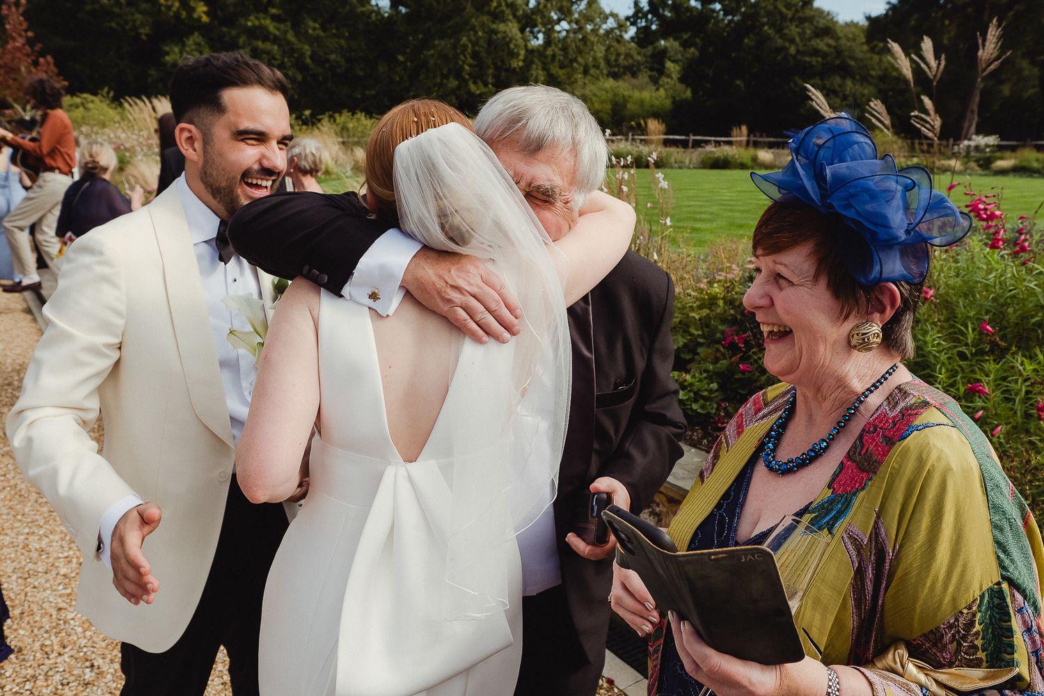 Wedding guests share joyful embraces and conversations during an outdoor celebration in a garden setting.