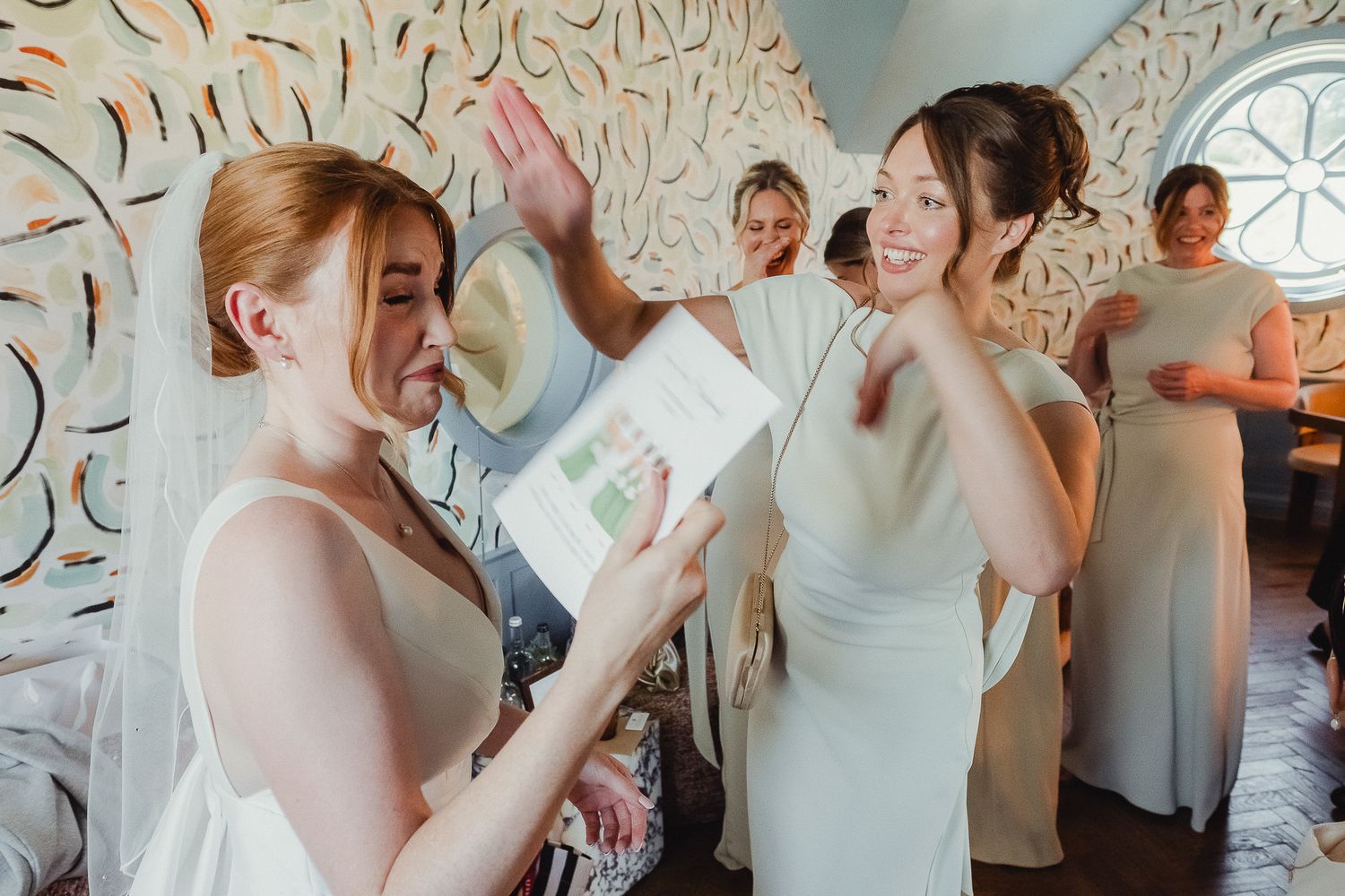 A group of people getting ready in a bridal suite with floral wallpaper and white decor.