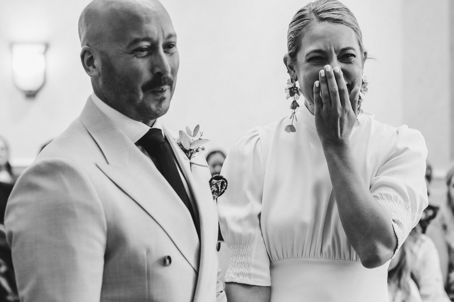 Black and white candid wedding photo showing an emotional moment between two people in elegant attire at their ceremony.