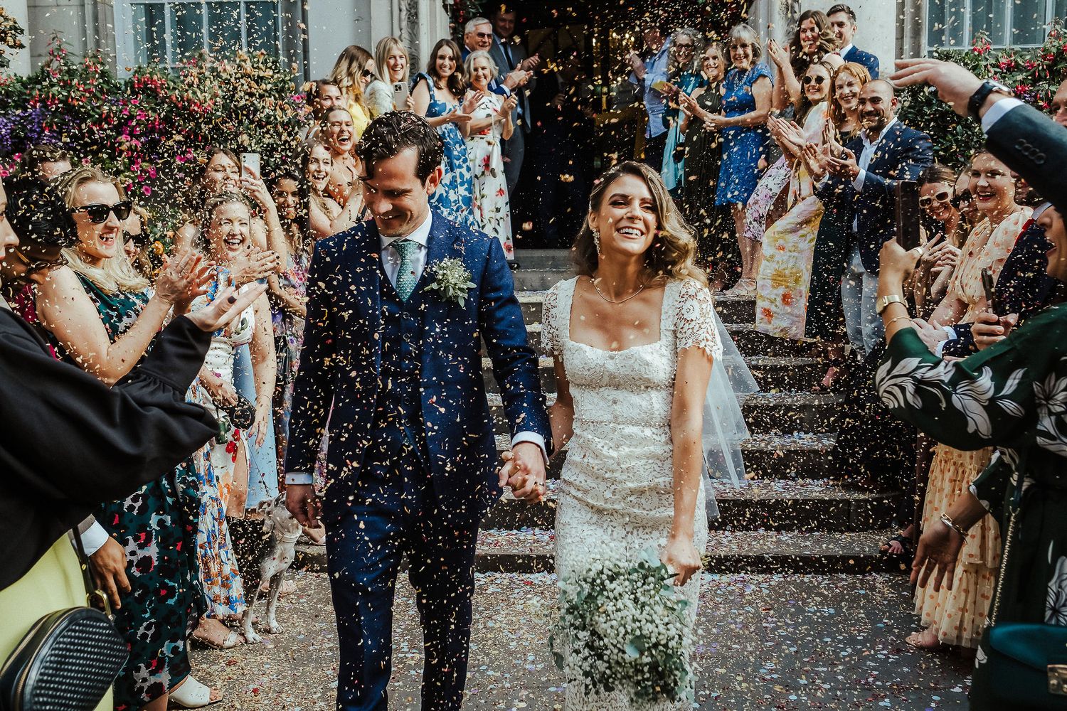 Wedding guests shower a happy couple with blue confetti during their joyful outdoor celebration.