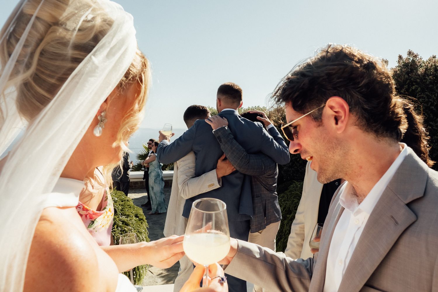 Bride and groom toasting with white wine glasses at outdoor wedding reception on sunny day.
