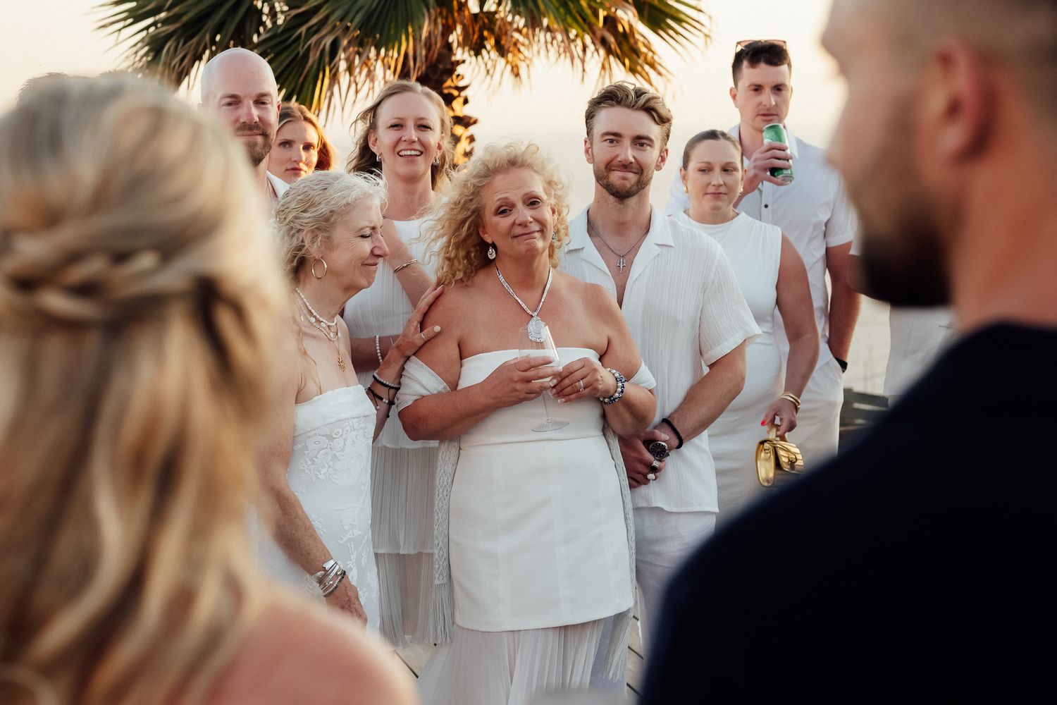 Guests smiling and celebrating at an outdoor beach wedding ceremony during golden hour sunset.