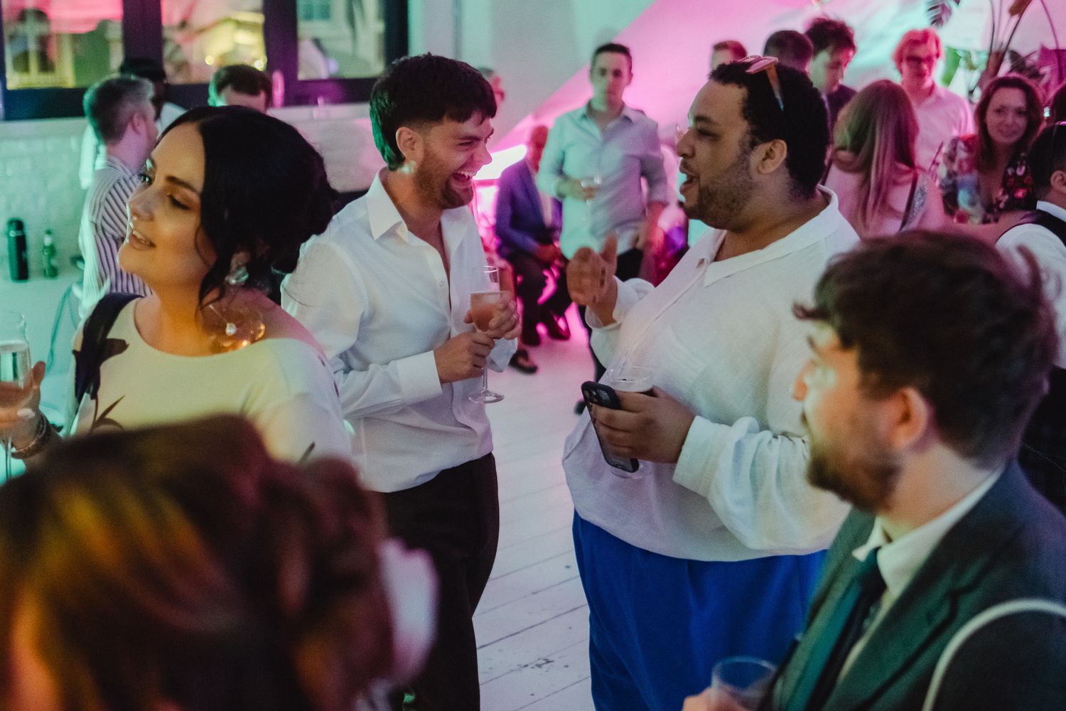 A group of people dancing and celebrating at a festive indoor event with colorful lighting.