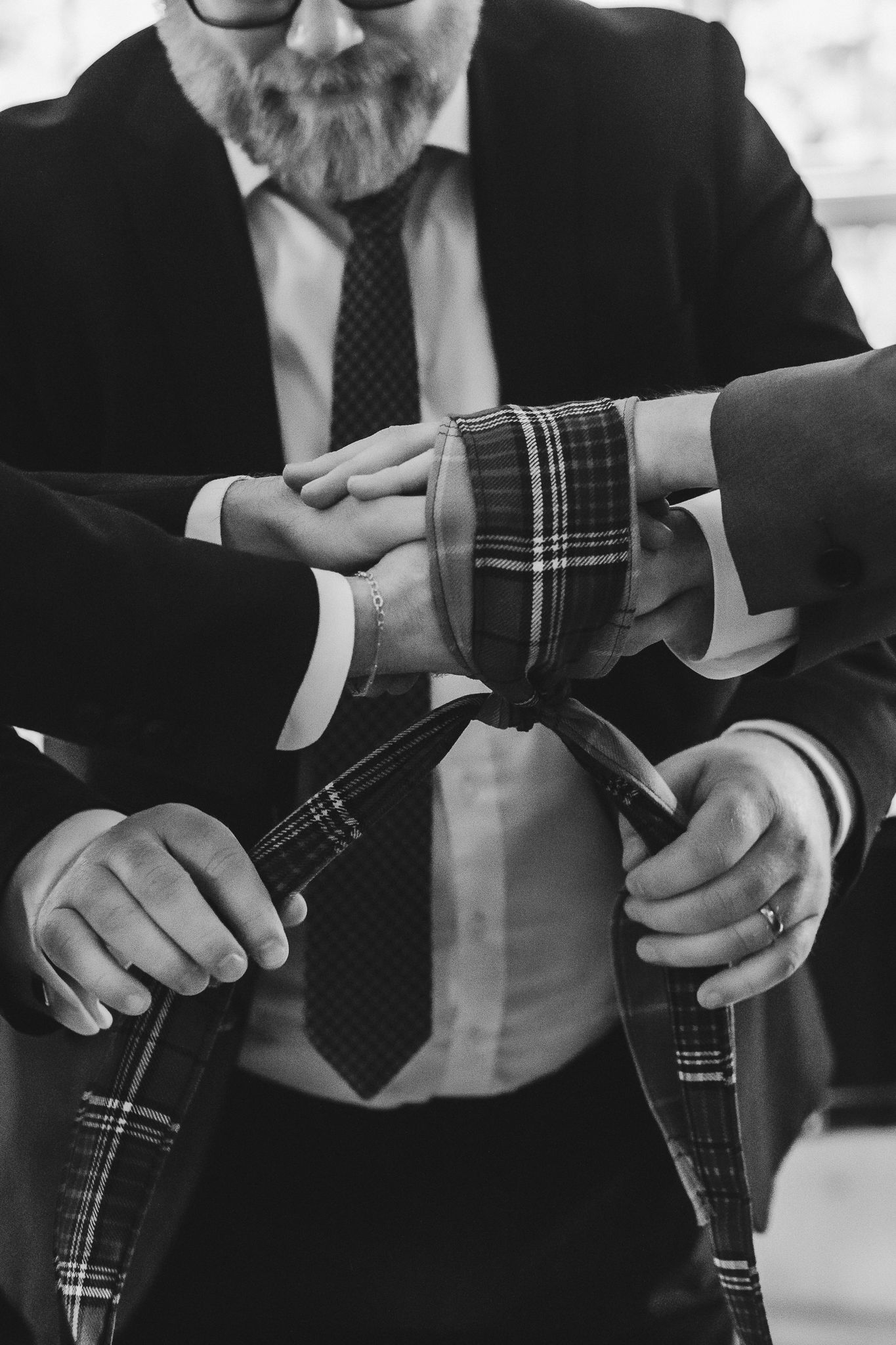 Close-up sequence of hands in formal attire adjusting a plaid patterned necktie against a black suit.