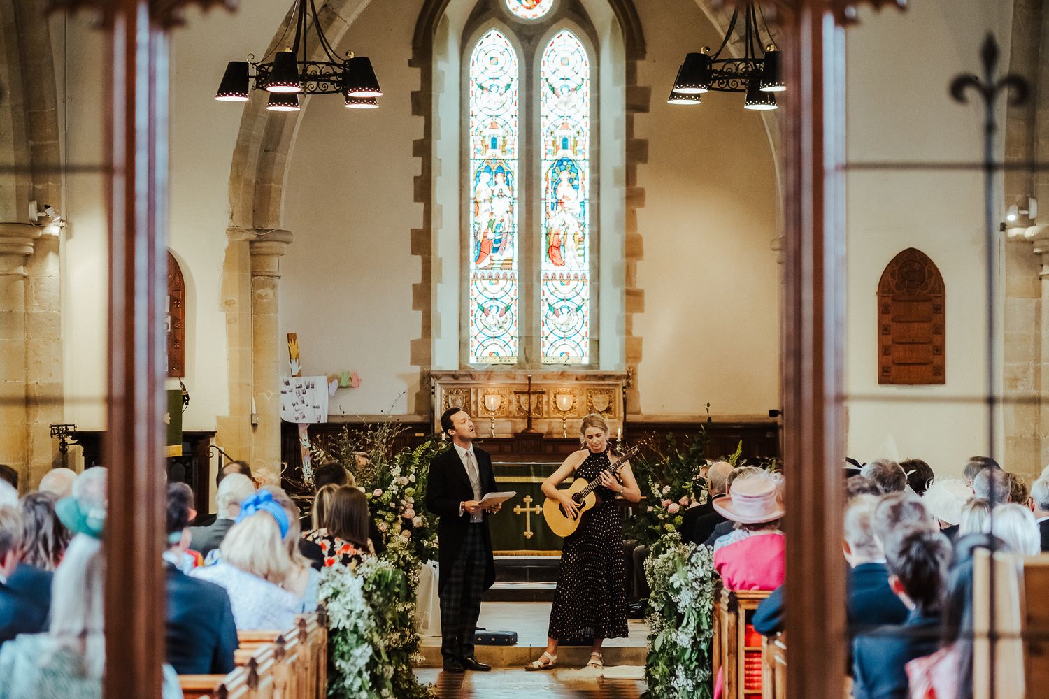 Church wedding ceremony setting with musicians performing and floral decorations along the aisle.