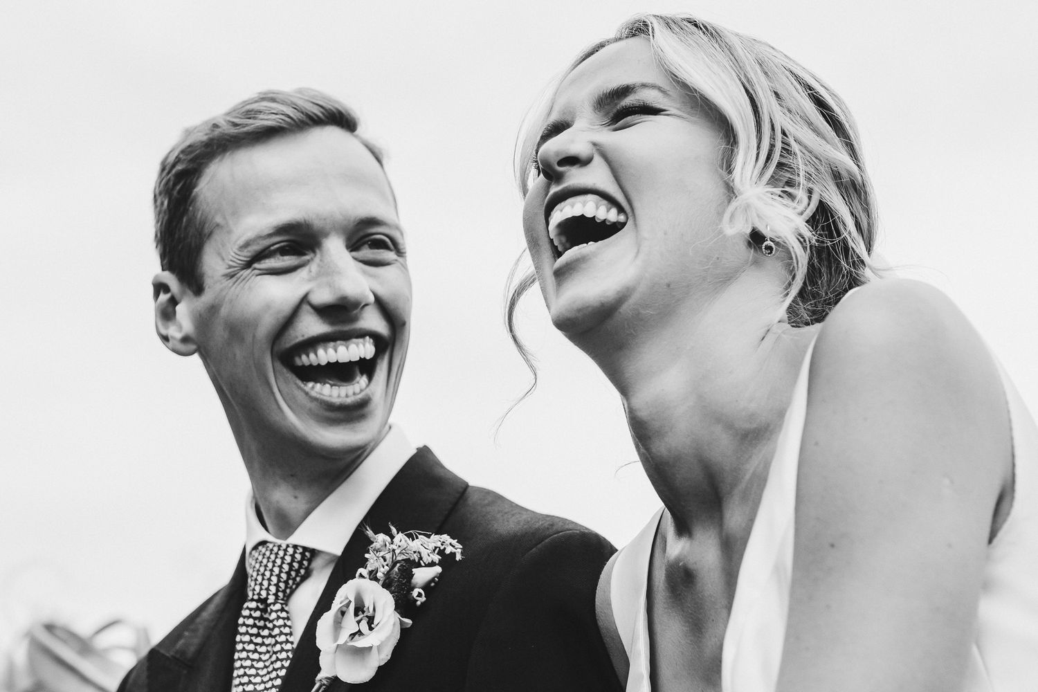 A black and white portrait capturing genuine laughter during a wedding celebration.