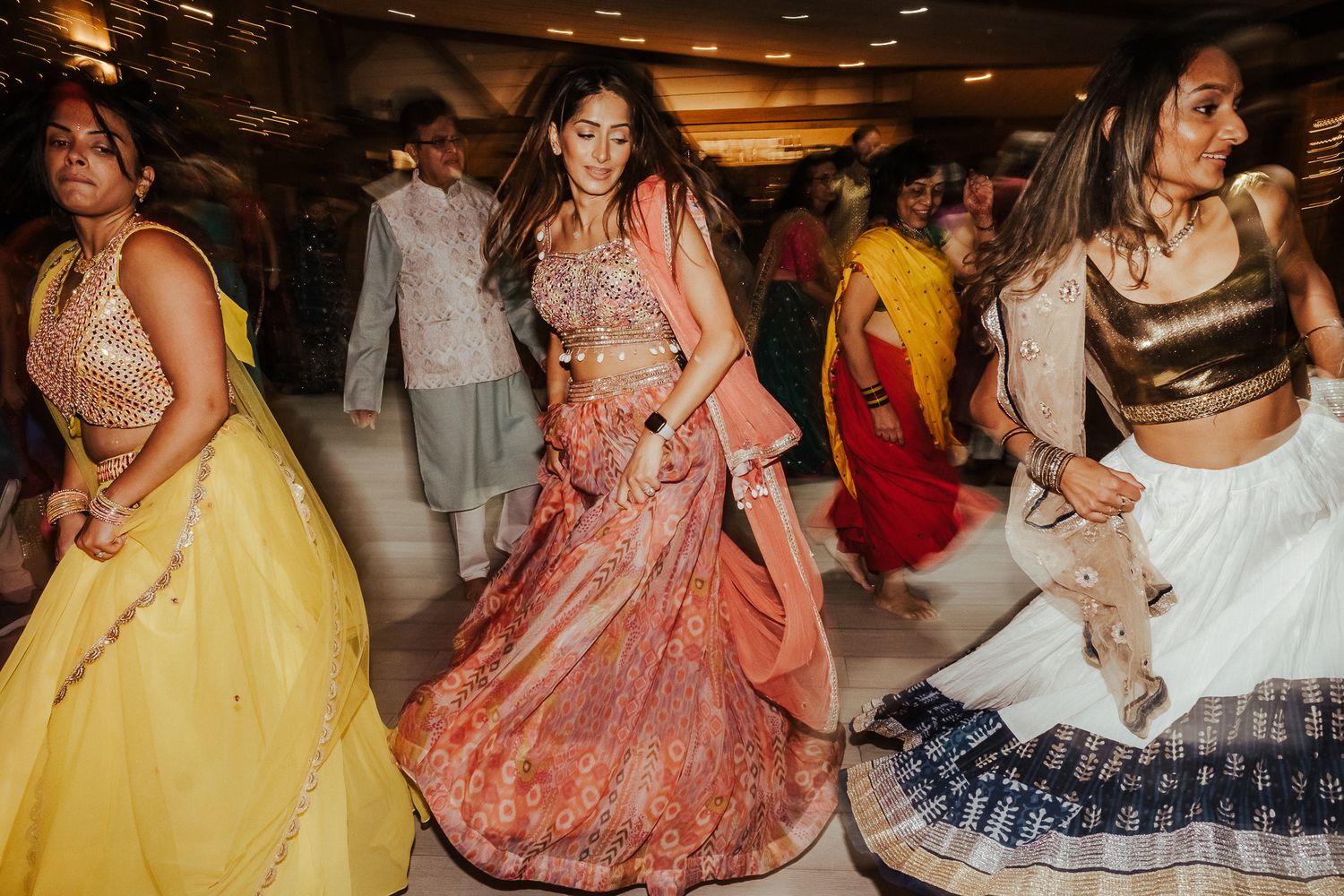 Wedding guests in colorful traditional Indian outfits dancing at a celebration.