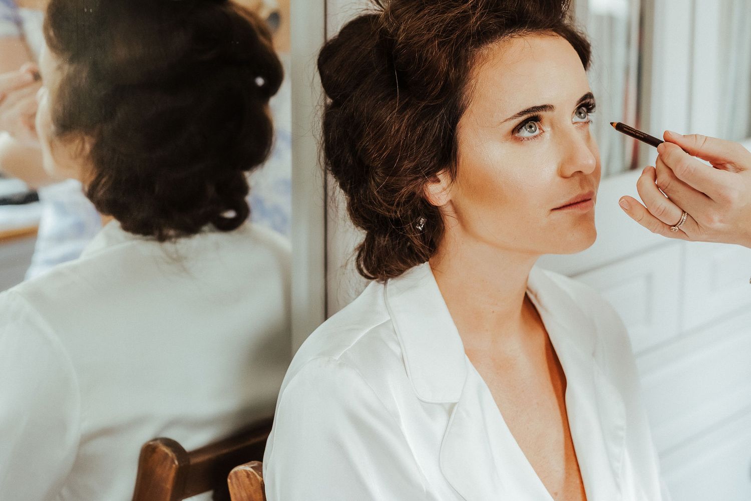 Close-up of wedding makeup application in a bright room with mirror reflection.