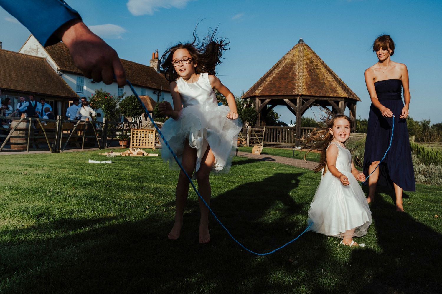 Playful moment of jumping rope at an outdoor wedding celebration with a gazebo in the background.
