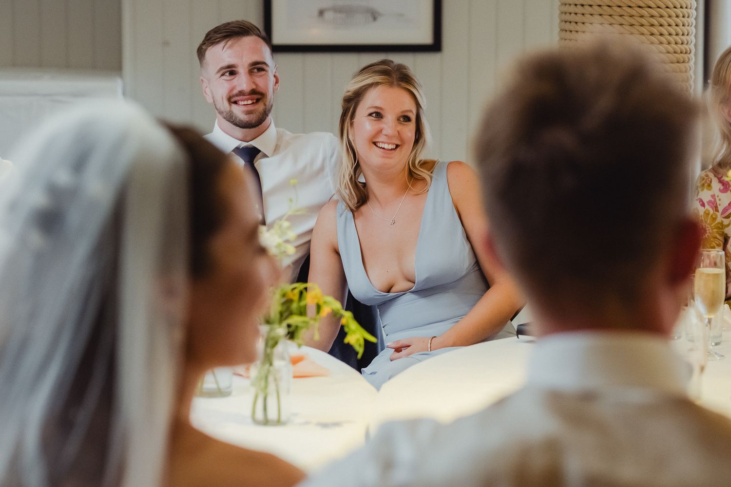 Wedding reception guests smile and laugh during speeches at an elegant indoor celebration.