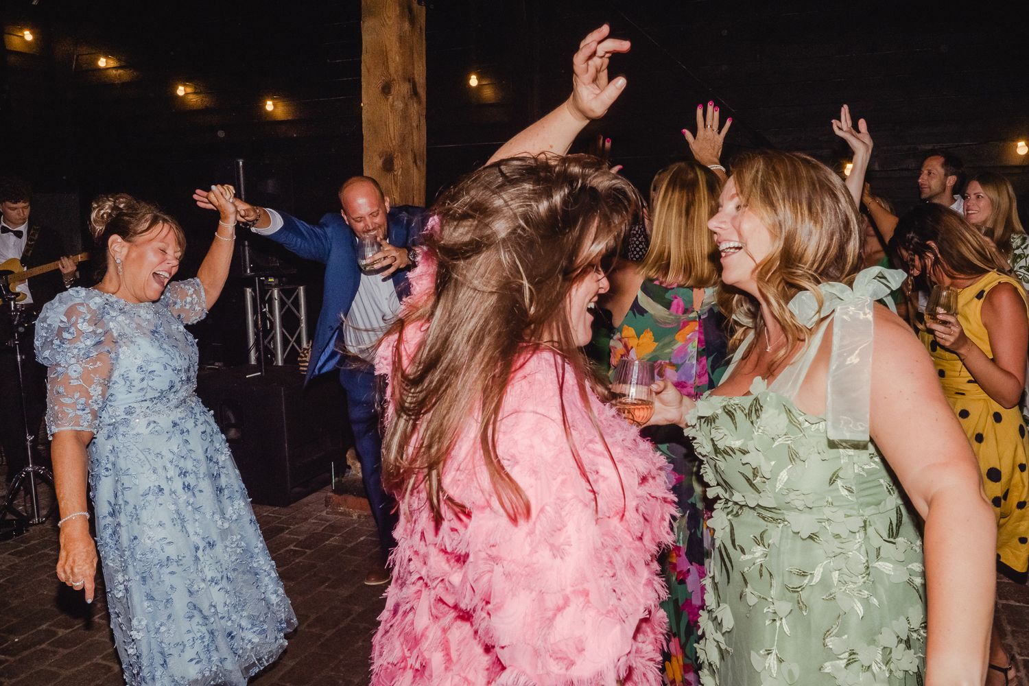 People dancing together at a lively party with colorful dresses and festive lighting in the background.