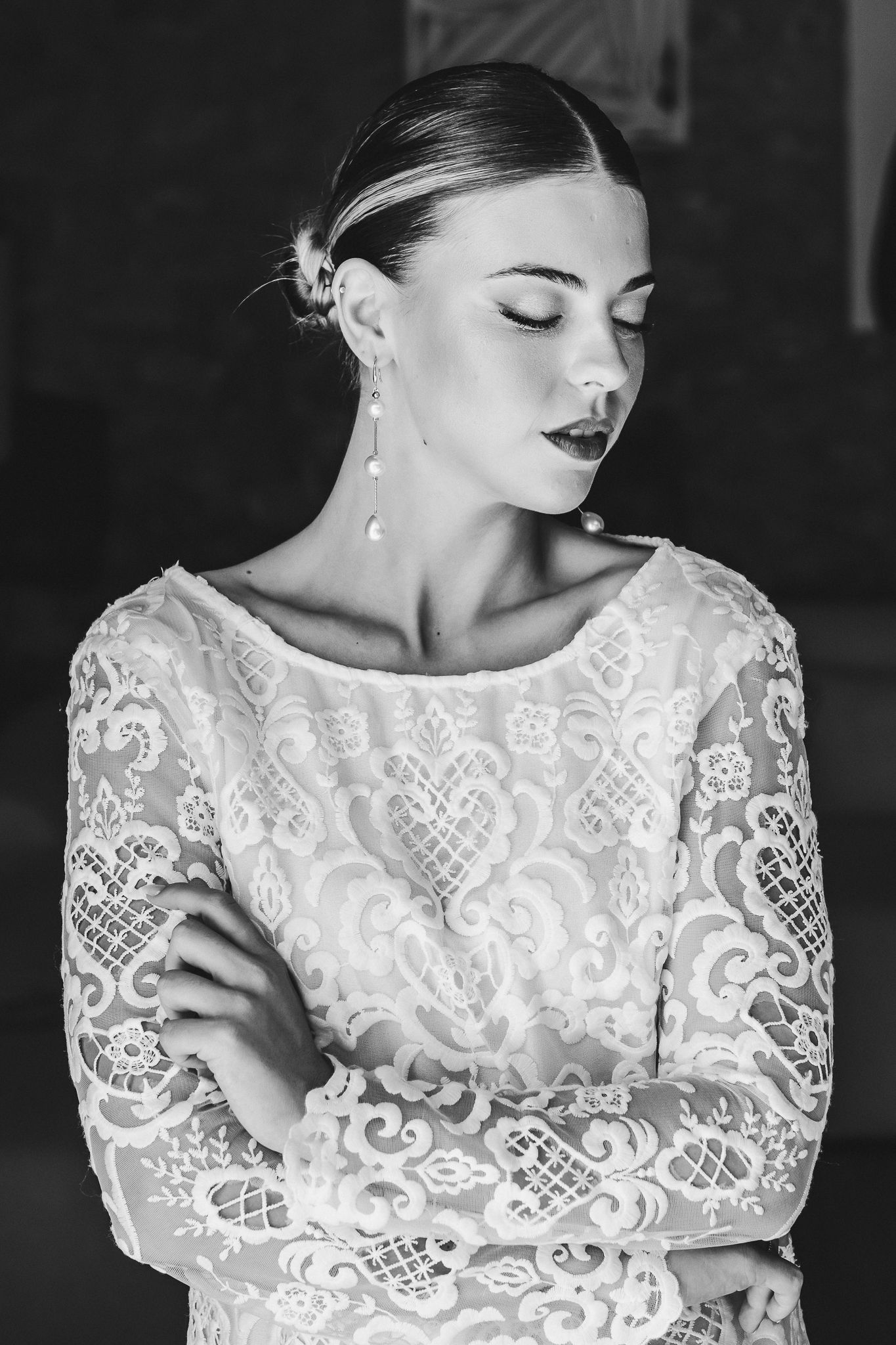 Black and white portrait of a bride in an elegant lace long sleeve wedding dress with eyes closed and pearl earrings.