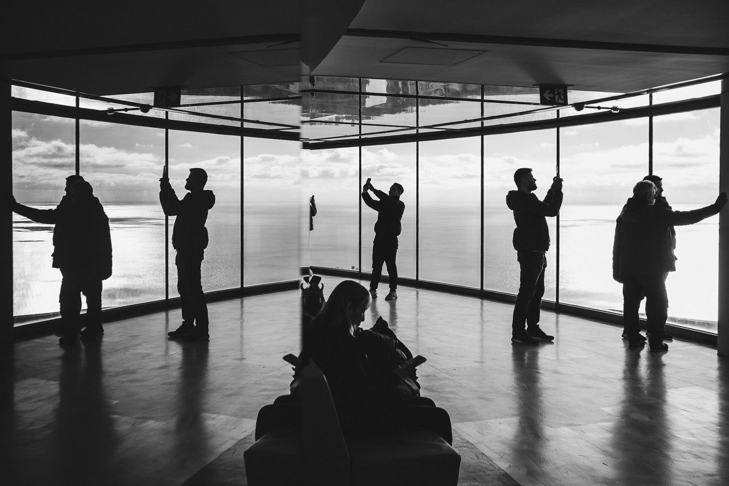 Silhouettes of people standing at observation deck windows against a bright sky background.