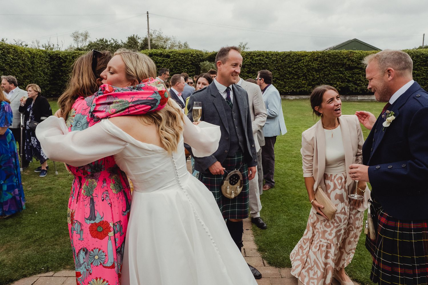 Wedding guests celebrate and dance together in a joyful outdoor reception on a green grassy field.