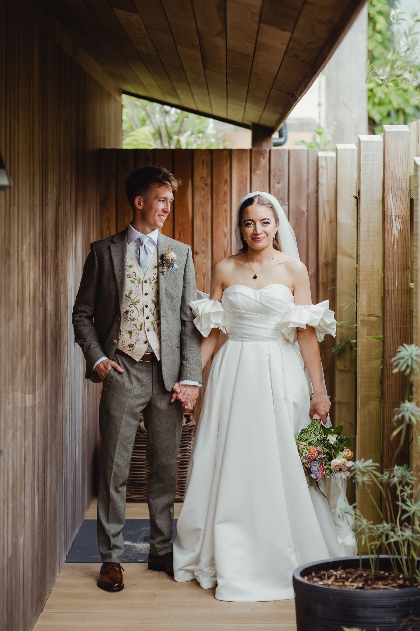 A couple shares a joyful moment walking together along a wooden walkway, with the bride wearing a flowing white gown.