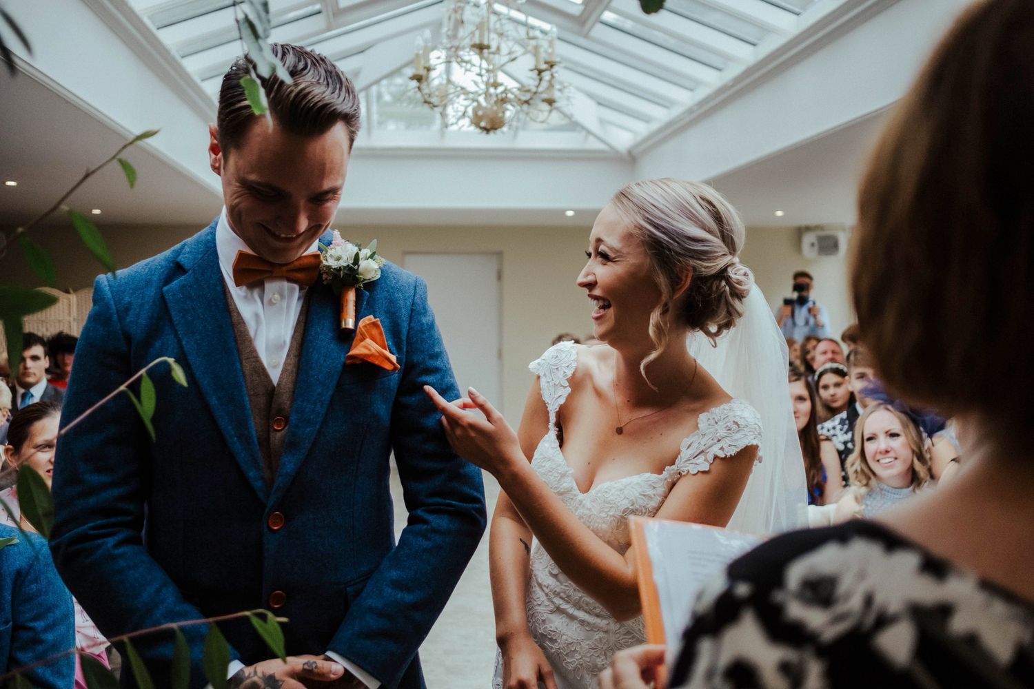 Couple sharing a joyful moment during their wedding ceremony in a sunlit conservatory.