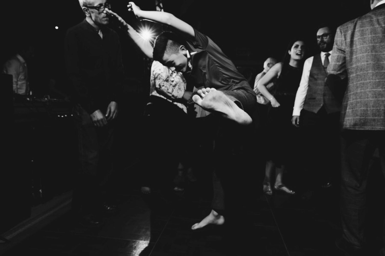 Dynamic black and white photo captures dancers mid-jump at wedding reception.