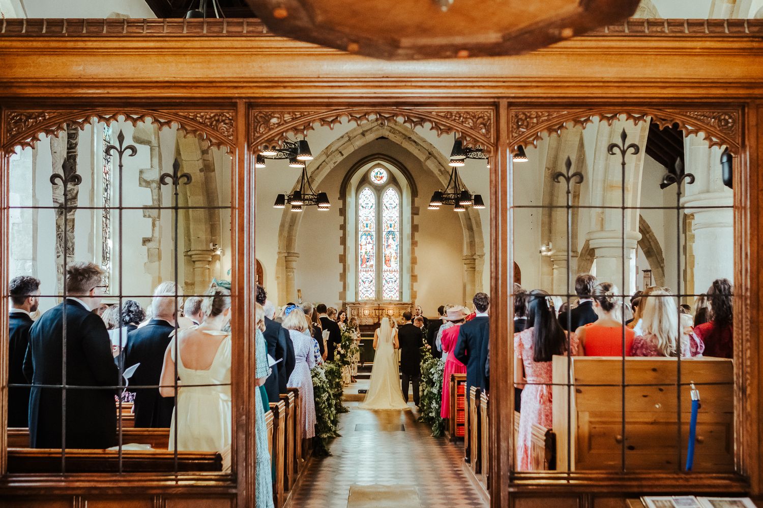 Wedding ceremony in ornate church with wooden pews and gothic architectural details.