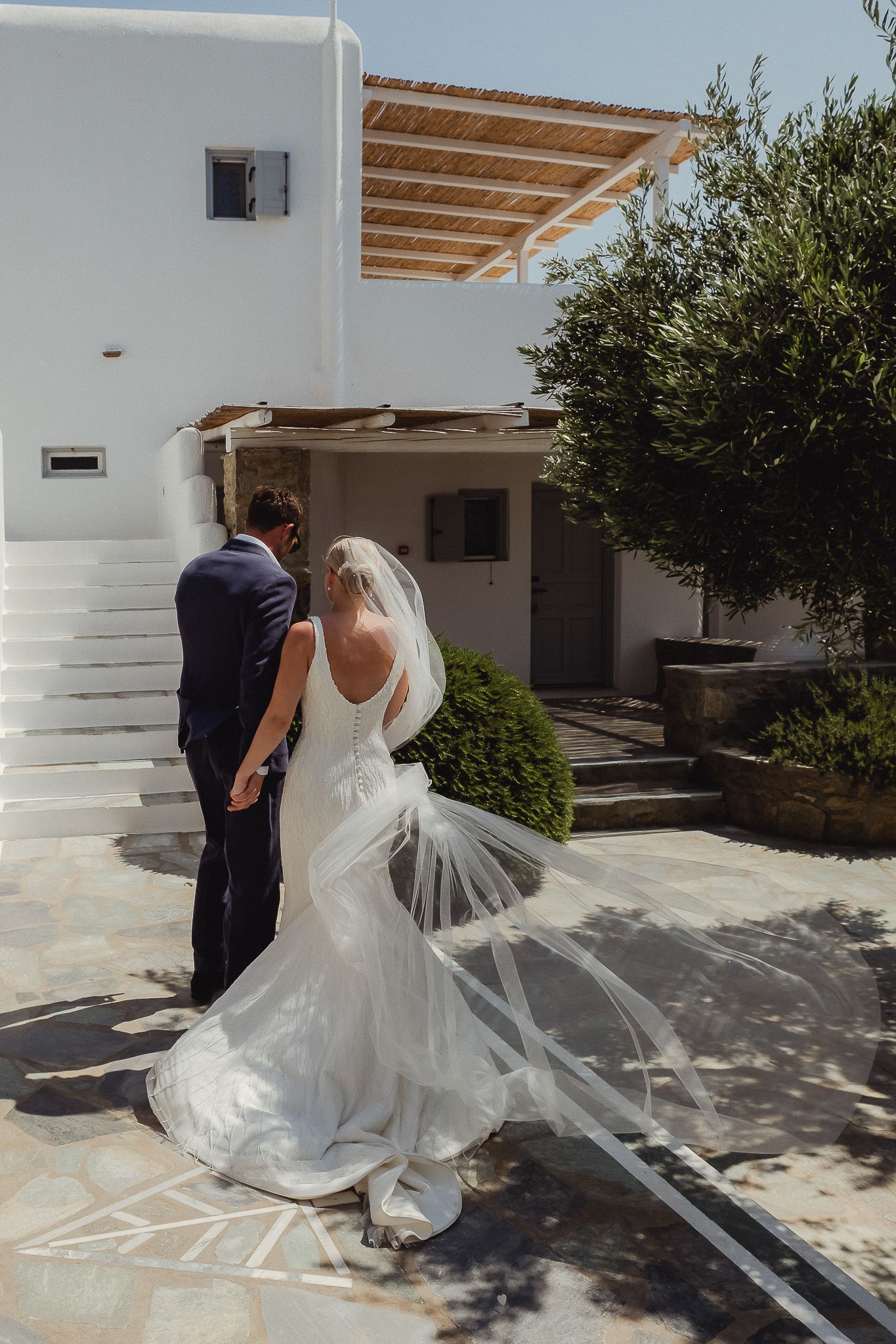 A romantic wedding photoshoot in a Mediterranean courtyard with white walls and flowing veil catching the sunlight.