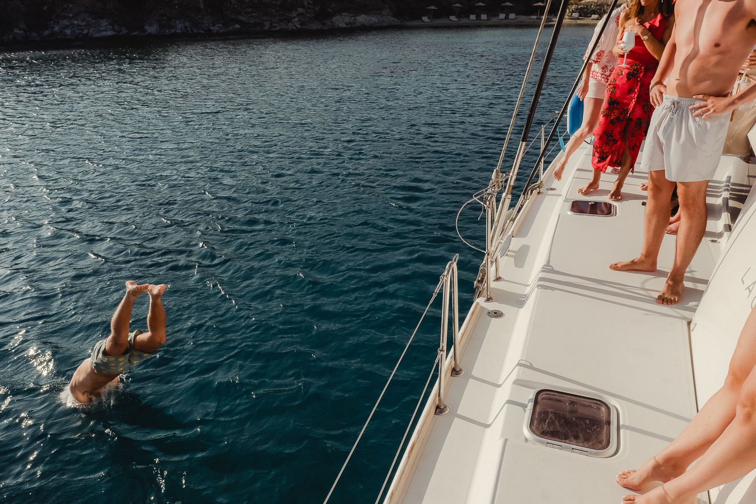 A person stands at the stern of a boat on calm blue waters during a sunny day.