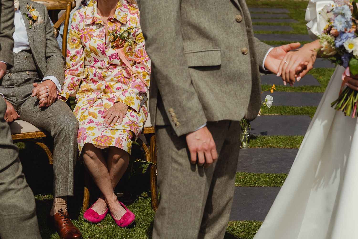 Wedding party members in floral dresses and grey suits standing together outdoors.