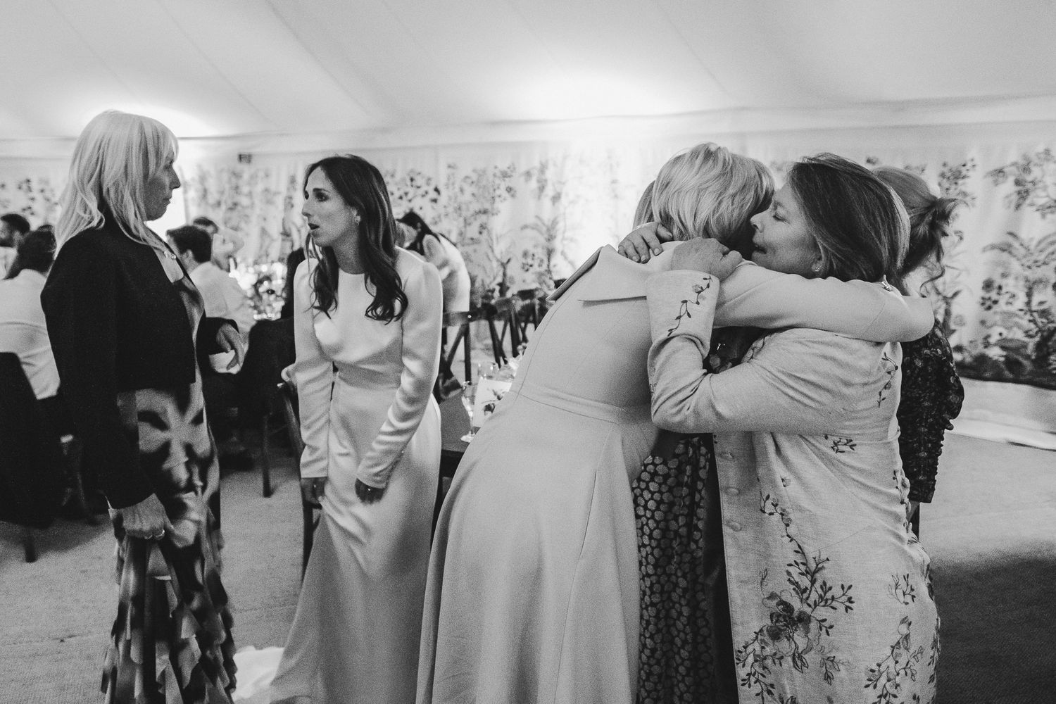 People dancing and embracing at a wedding reception in a white tent venue with a festive atmosphere.