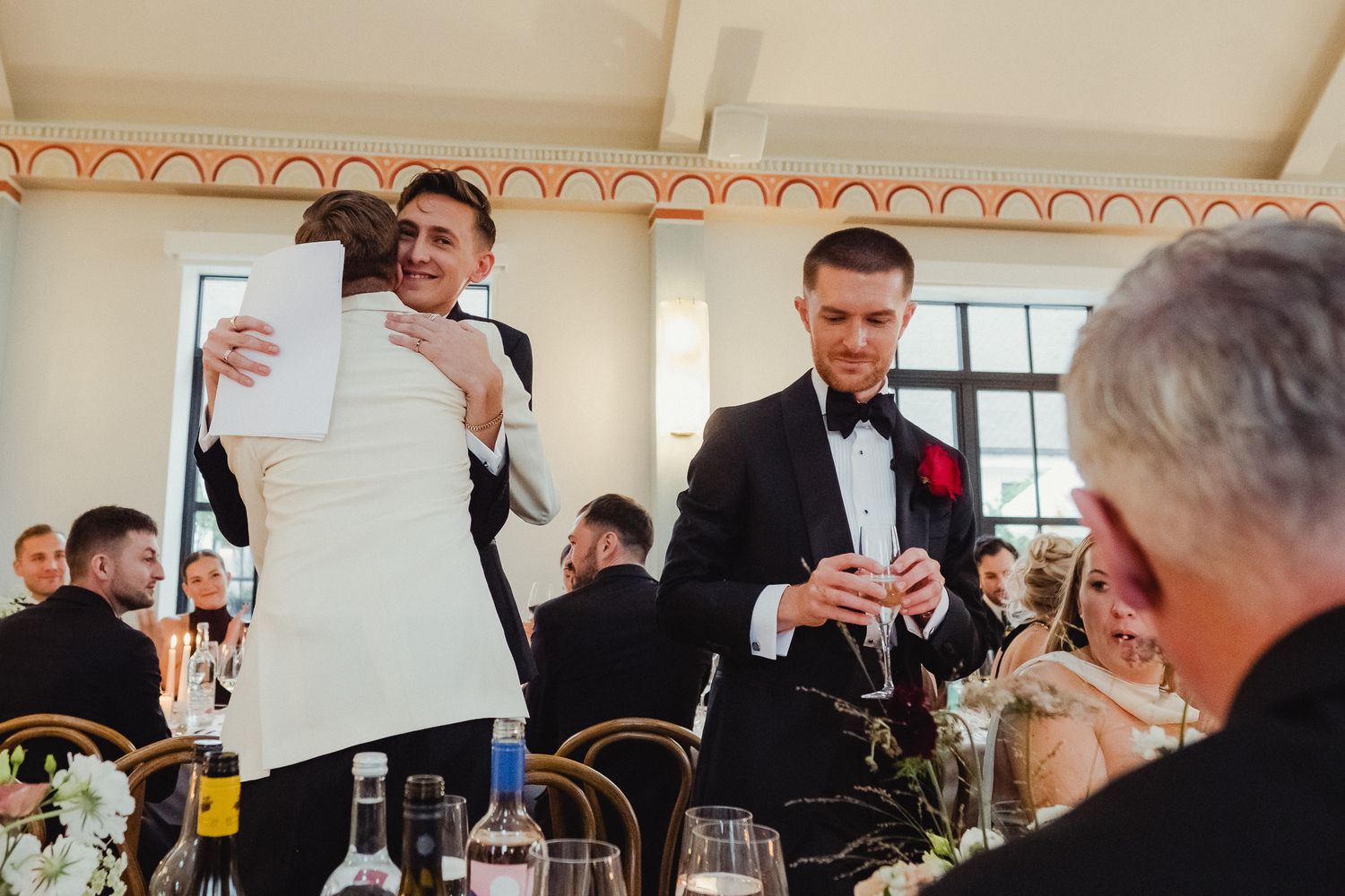 Wedding guests gathered around a dining table while speakers deliver toasts during an elegant reception celebration.