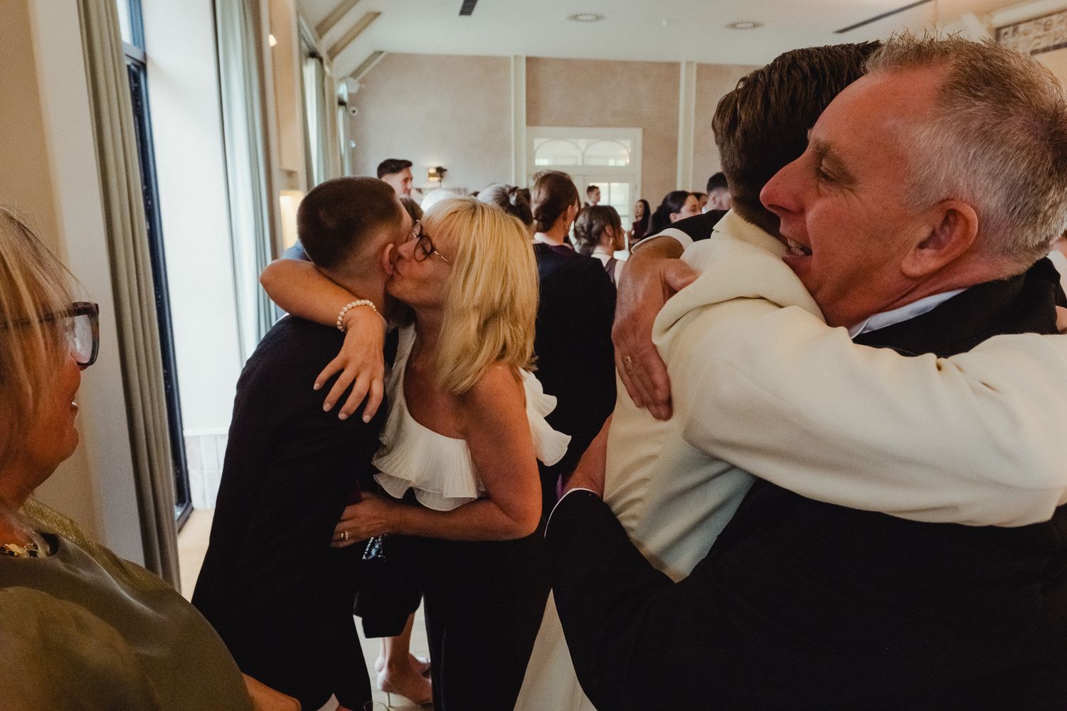 People embrace and hug each other emotionally in a bright indoor hallway during what appears to be a special occasion.