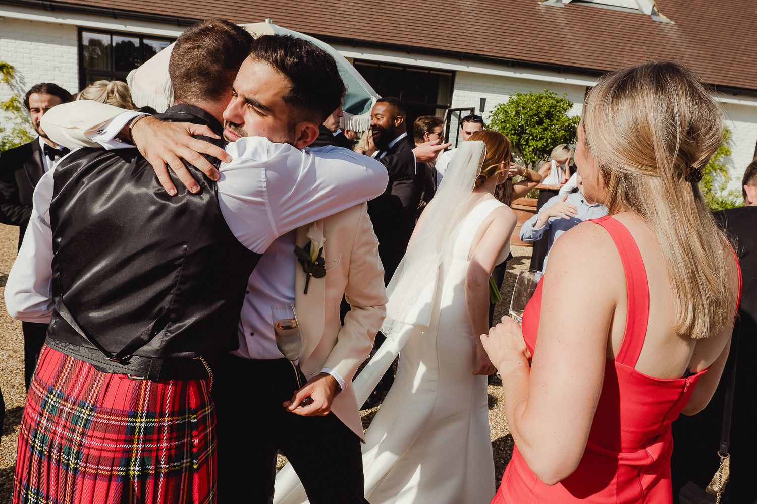 Two people share an emotional embrace at a wedding celebration while others look on.