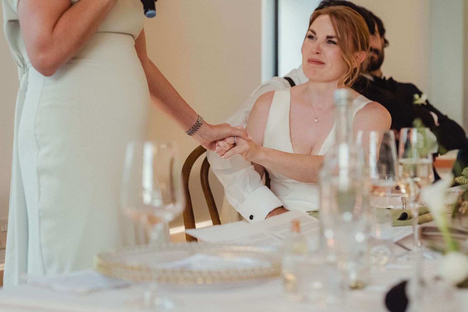 Wedding guests enjoy a meal and conversation at an elegant reception dinner table with white linens and glassware.