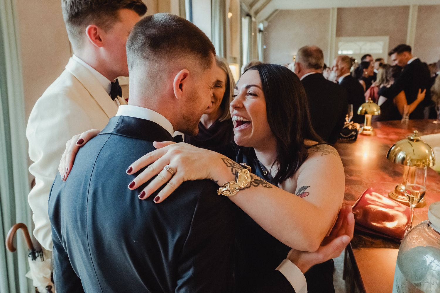 Wedding guests dance and celebrate together during a lively reception in an elegant venue with large windows.