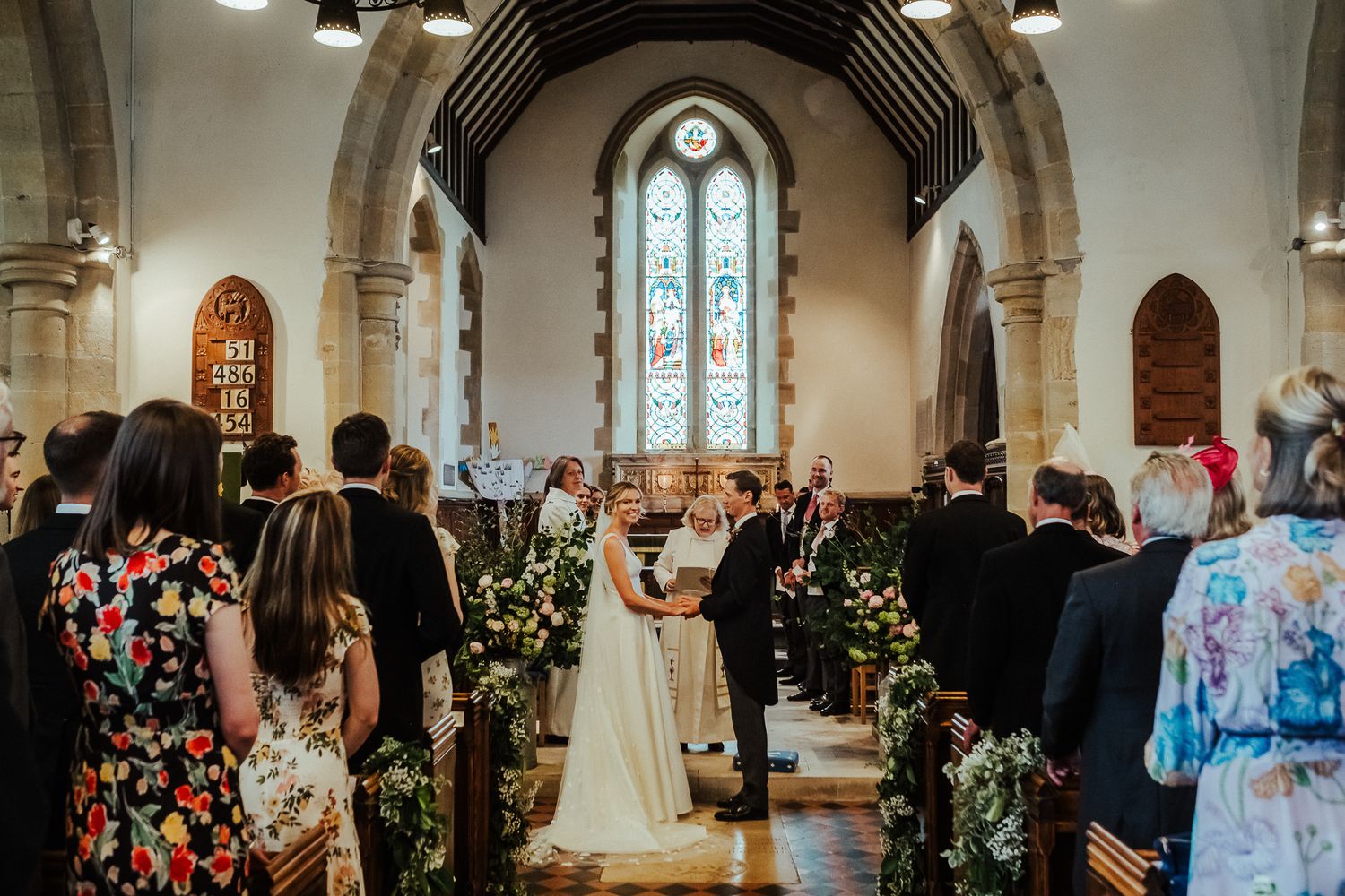 Church wedding ceremony with floral decorations and guests in colorful attire.