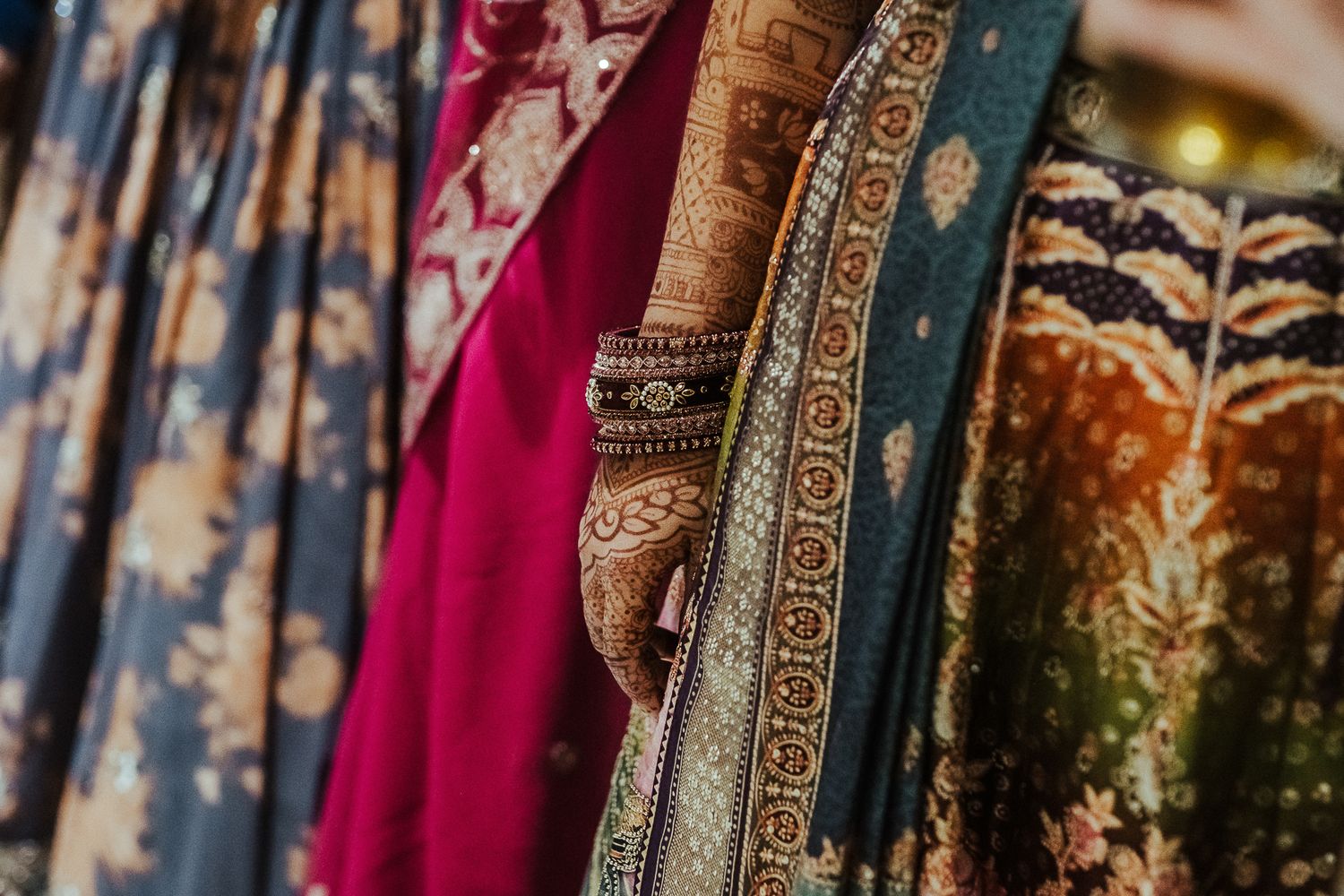 Close-up detail of ornate embroidered saris in rich jewel tones with intricate border designs.