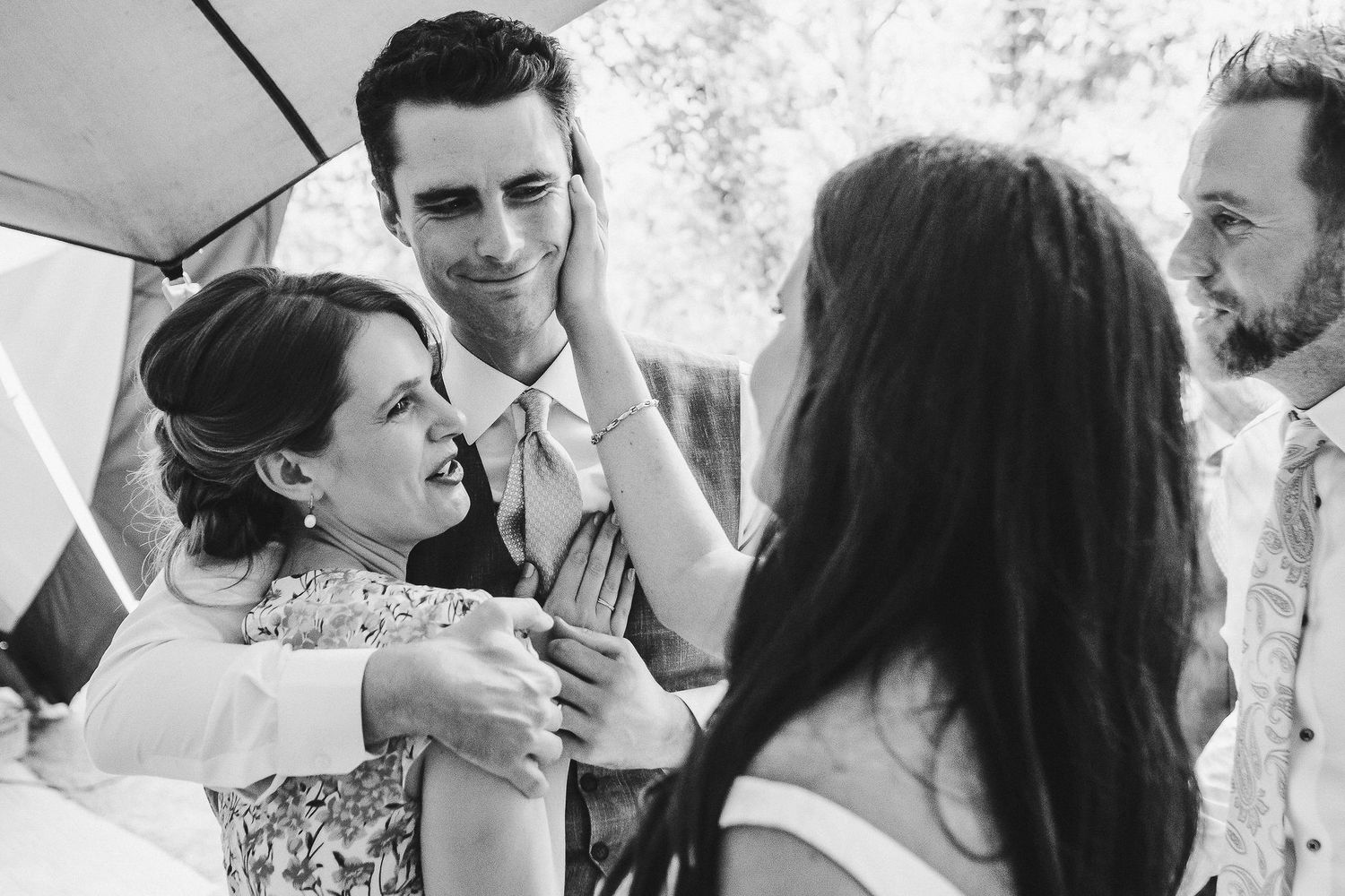 Wedding party members embrace and laugh together during a candid moment.