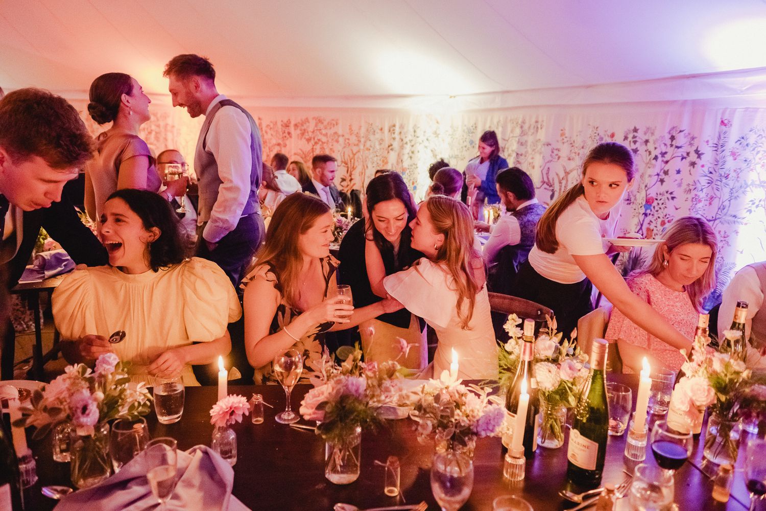Wedding guests dance and celebrate on a lively dance floor under decorative lighting at an evening reception.