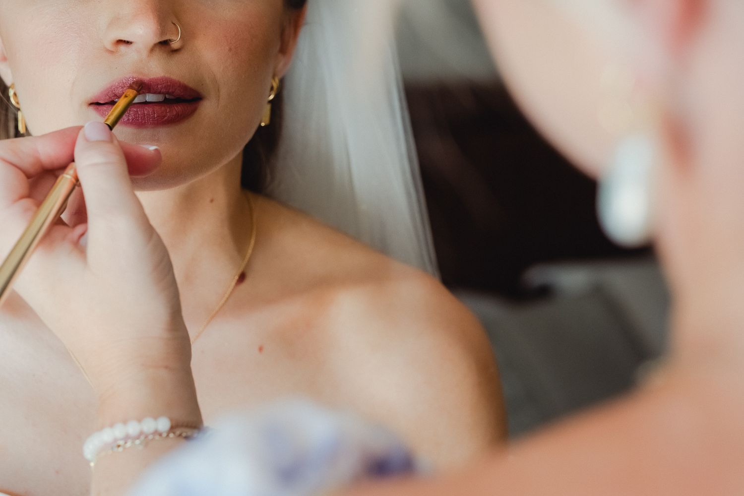 A close-up photo shows plump, glossy lips with shimmering pink lipstick and a delicate nose piercing.