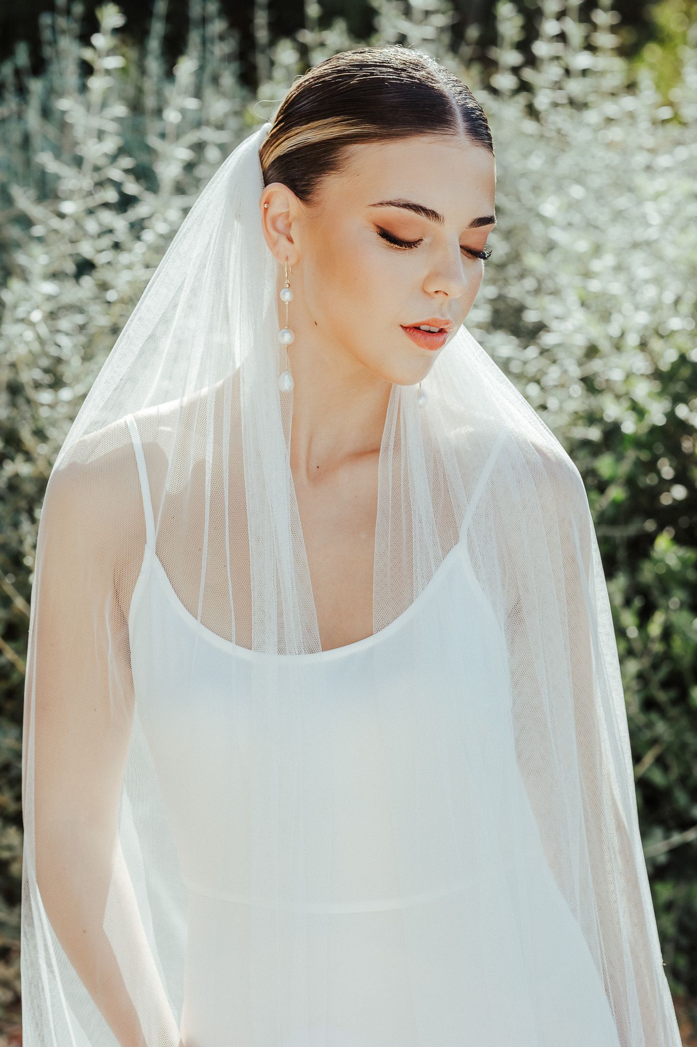 A bride in a white wedding dress and veil poses in front of cascading white floral decorations in an outdoor setting.