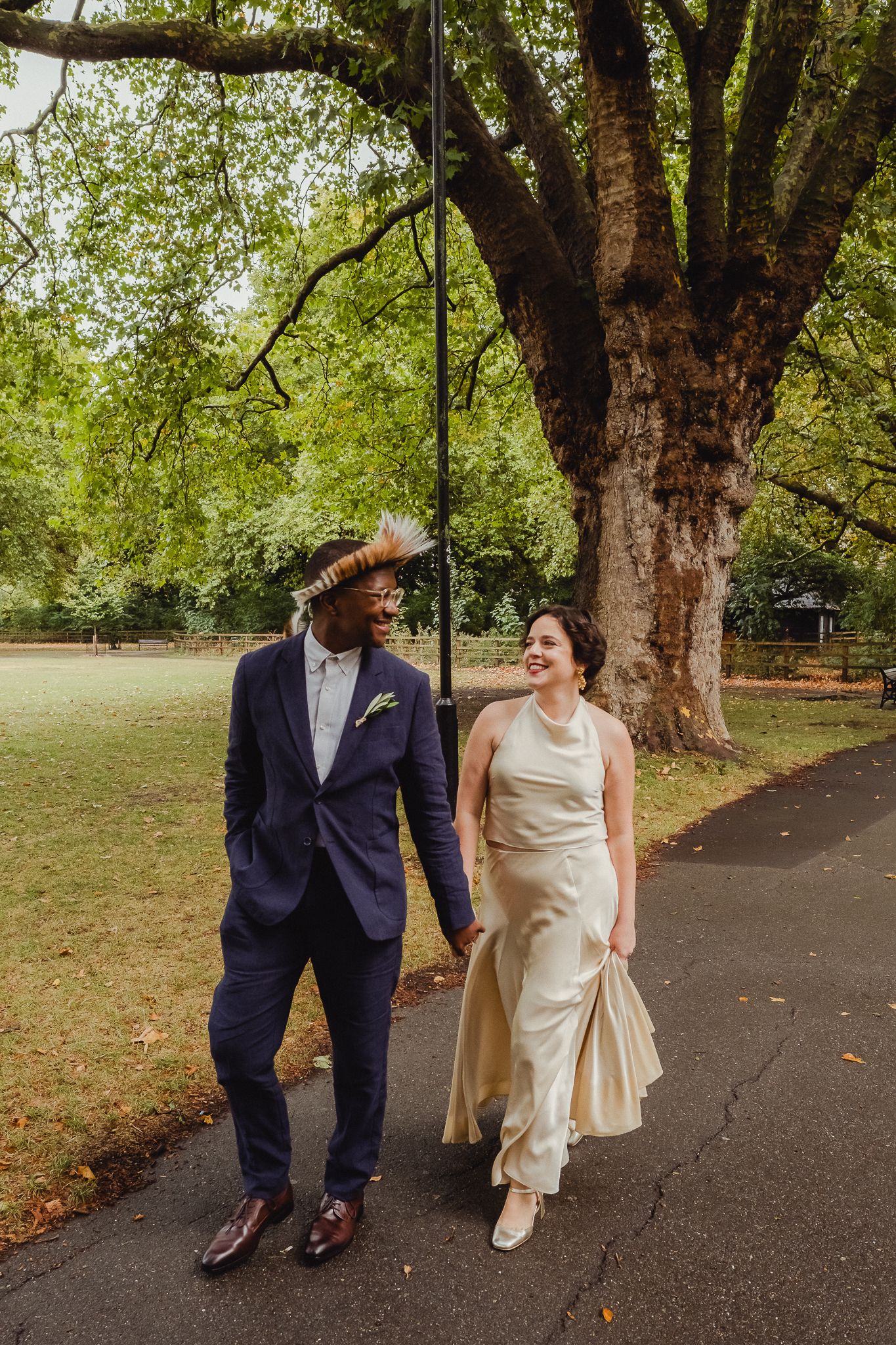 A couple walks together on a tree-lined path during an autumn wedding photoshoot.