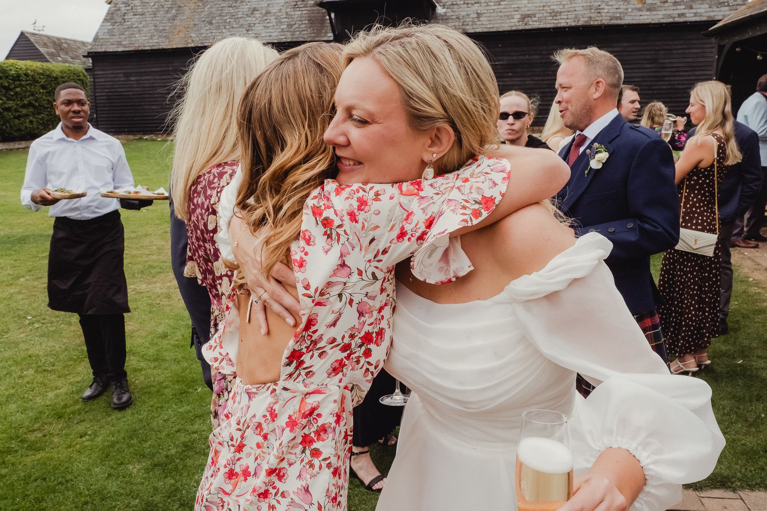 Wedding guests gather outdoors for a celebratory moment with the bride in a flowing white dress.
